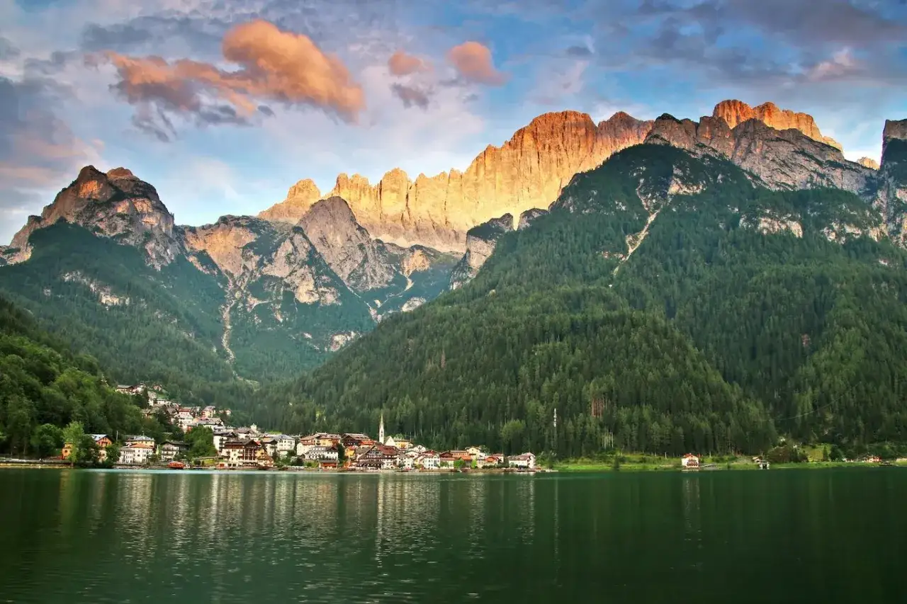 Un incantevole giro del lago di Alleghe con montagne maestose illuminate dal sole al tramonto e un villaggio pittoresco che si specchia sull'acqua.