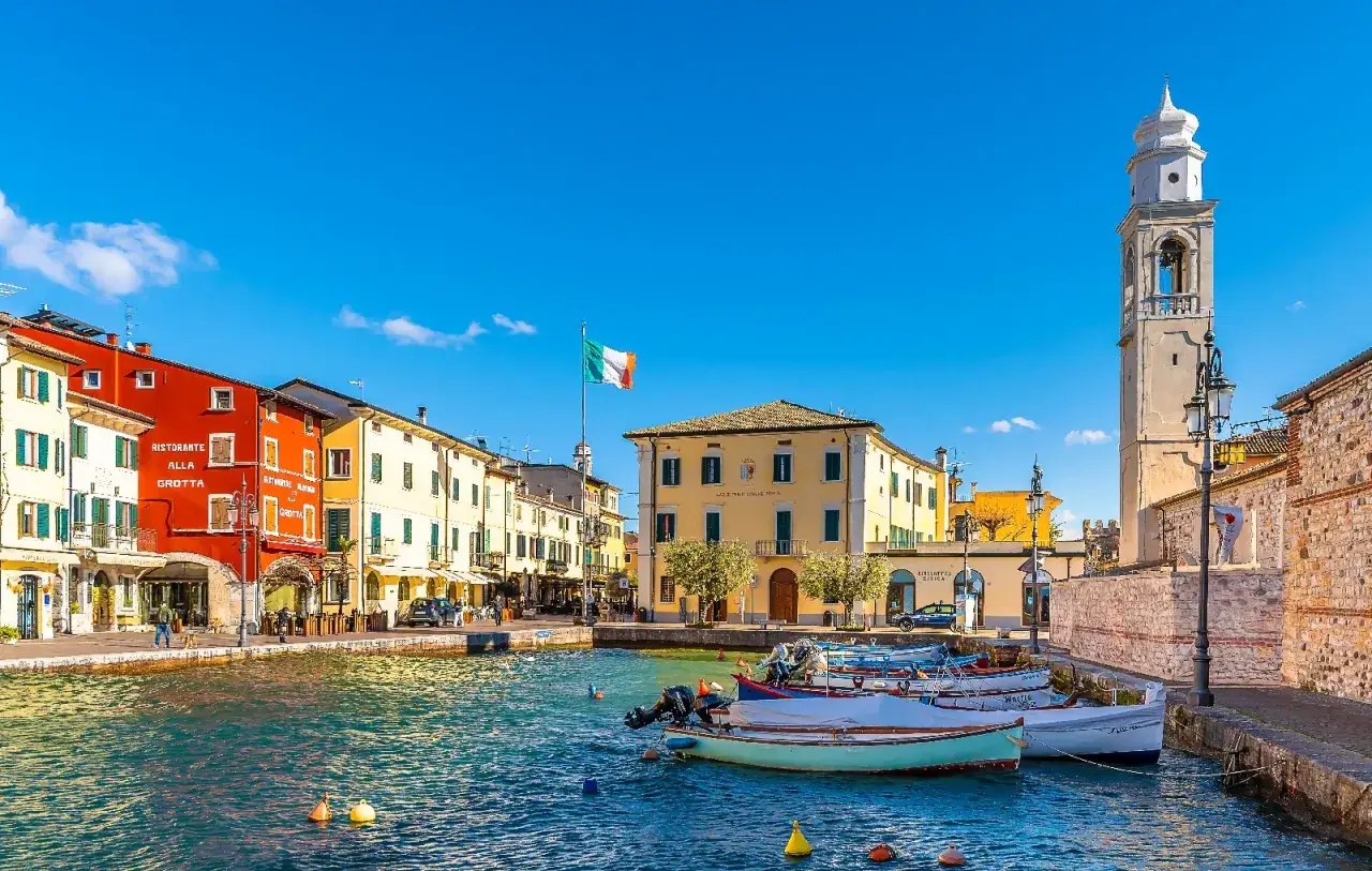 Un pittoresco porto con case colorate e un campanile, dove si trova Lazise, sul Lago di Garda.
