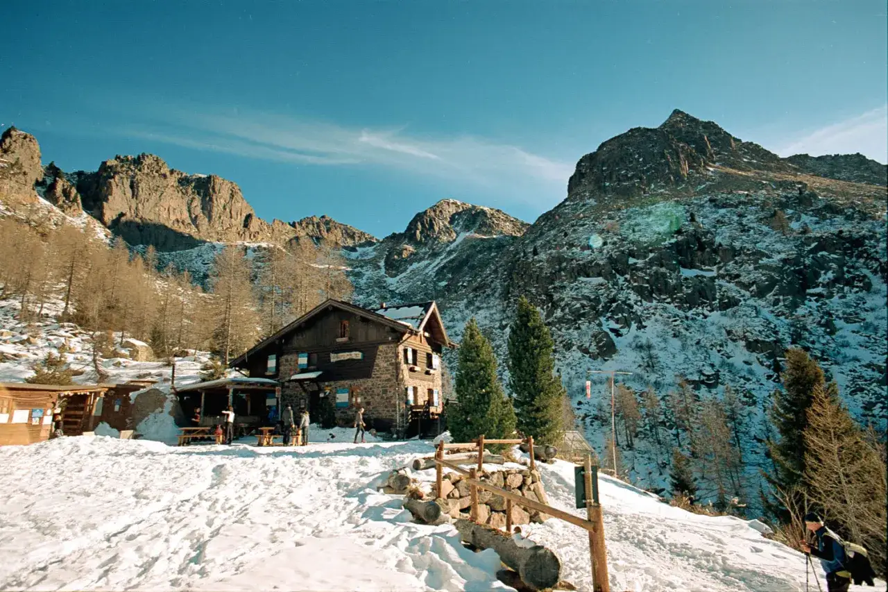 Rifugio Sette Selle innevato, con montagne sullo sfondo. Un sentiero battuto indica come arrivare.