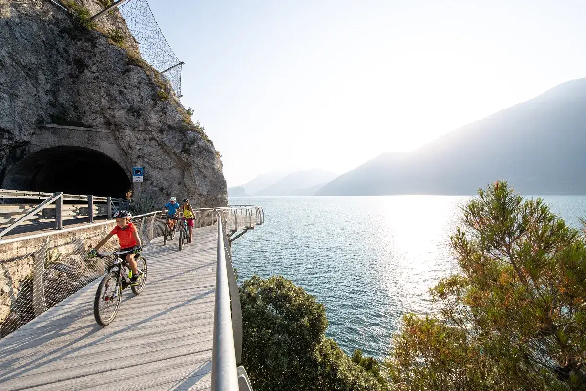 Ciclisti su una pista ciclabile panoramica sul lago, con un tunnel scavato nella roccia. Un'emozionante avventura per il giro lago di Garda.