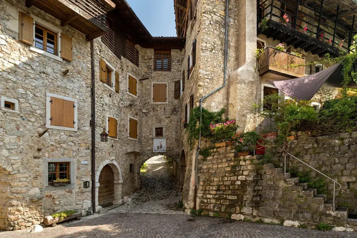 Un vicolo acciottolato tra antiche case in pietra, un esempio di borghi da visitare in Trentino, con fiori colorati e scorci suggestivi.