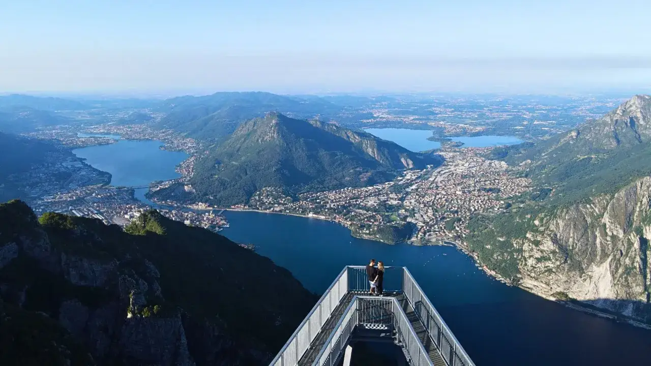 Coppia ammira il panorama mozzafiato del lago di Lecco da una passerella panoramica.