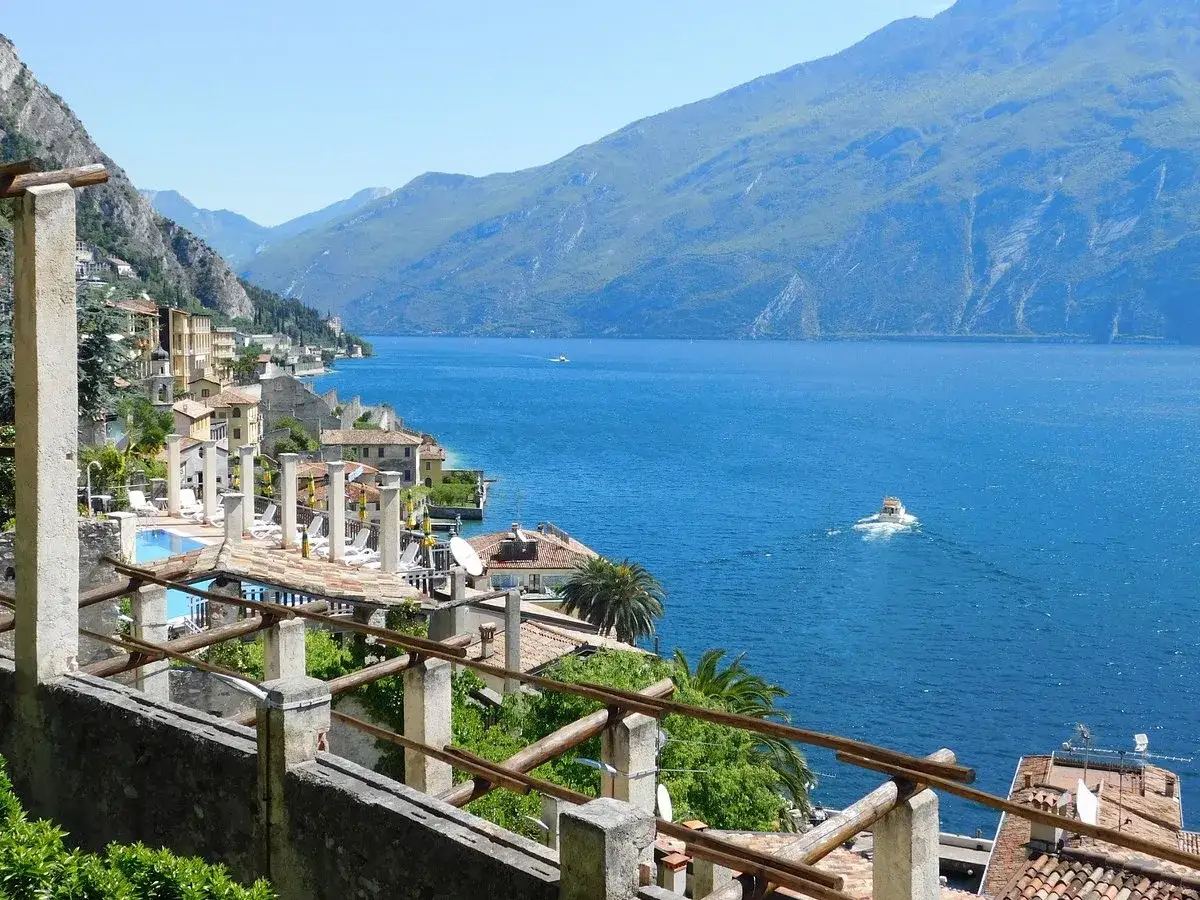 Vista panoramica di Limone sul Garda con il lago azzurro, montagne verdi e un battello in lontananza.