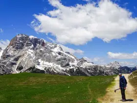 Un uomo con bastoncini da trekking su un sentiero in Trentino, con imponenti montagne innevate sullo sfondo. Un'esperienza di trekking trentino facile e panoramica.