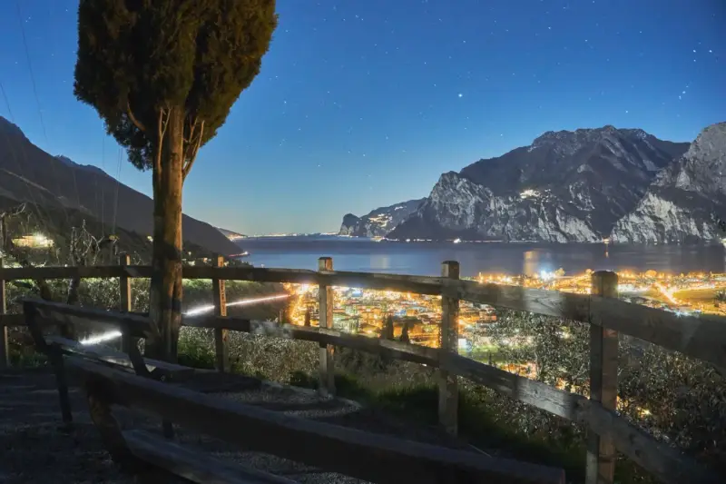 Peschiera del Garda di sera: un panorama mozzafiato con luci scintillanti, montagne imponenti e un cielo stellato. Ideale per una serata romantica.
