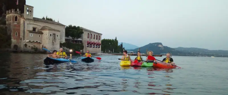Persone in kayak sul lago verde, con un antico edificio sullo sfondo, vicino a San Vigilio di Marebbe.