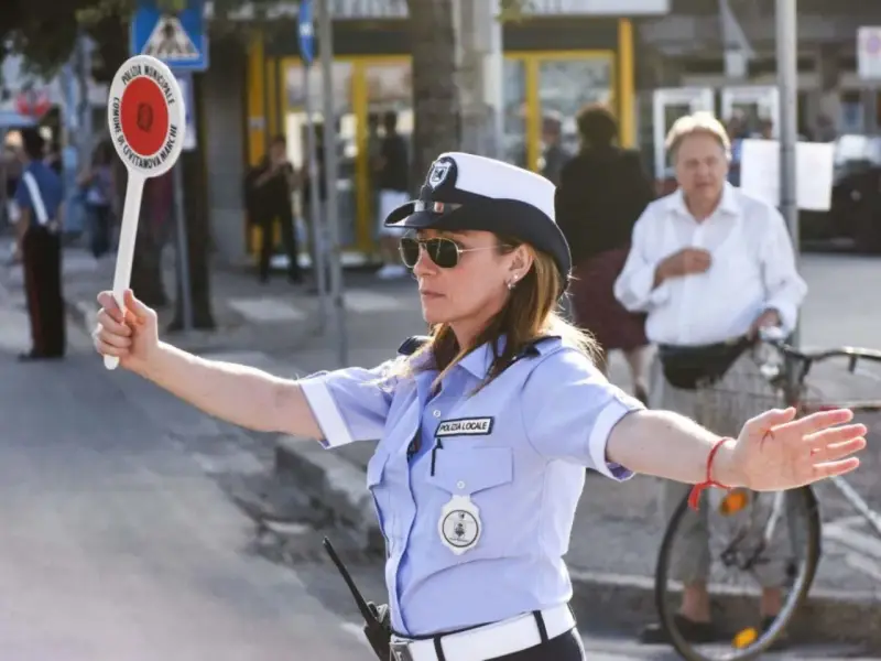 Agente di polizia locale in posizione vigile, braccio alzato per dirigere il traffico.