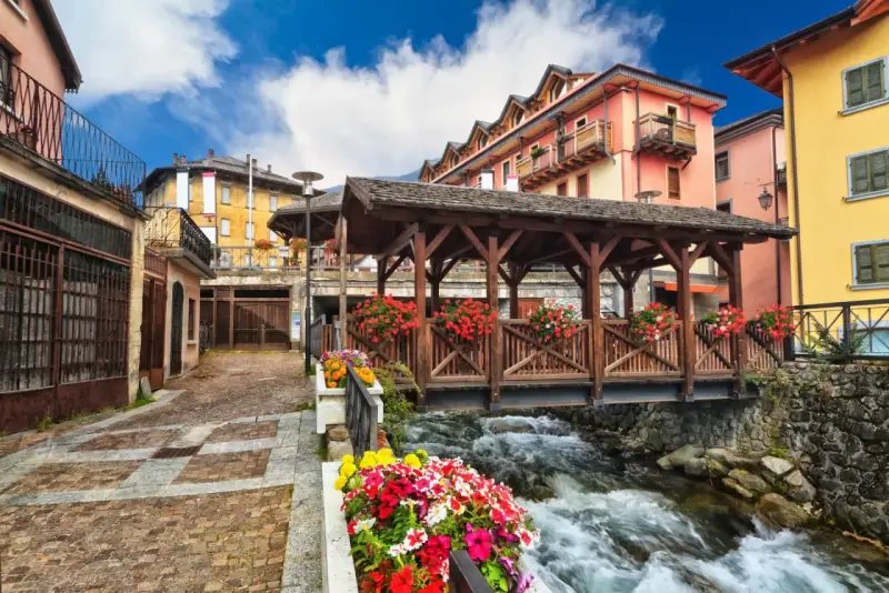 Un pittoresco ponte di legno coperto, adornato di fiori, attraversa un torrente impetuoso. Un incantevole scorcio di cosa vedere in un borgo alpino.
